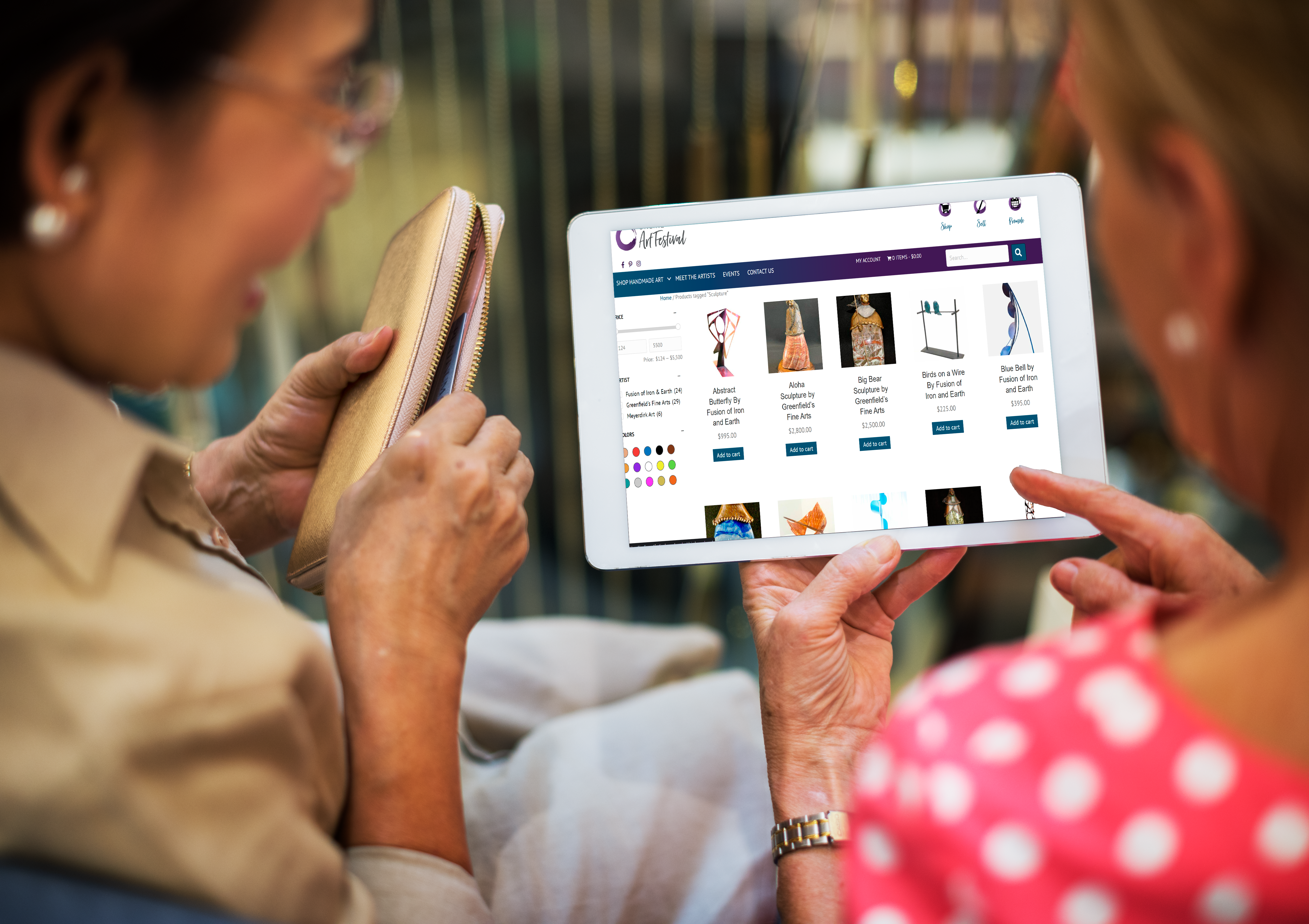 Women shopping for art at OAF on a tablet